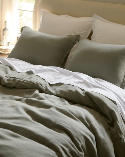 A bed with white cotton percale and moss green linen sheets