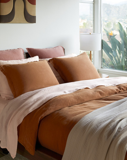 A bed made with orange, light pink, and cream linen bedding