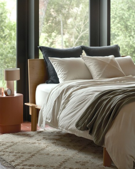A neatly made bed with decorative pillows and cream percale cotton sheets