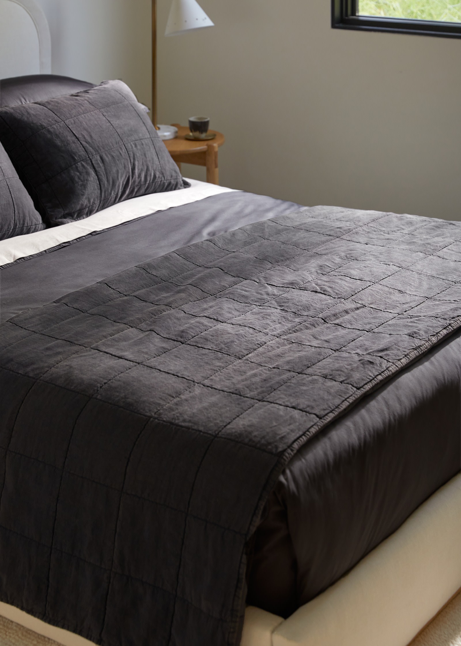 A dark grey coal linen quilt with a box pattern folded neatly at the foot of a bed