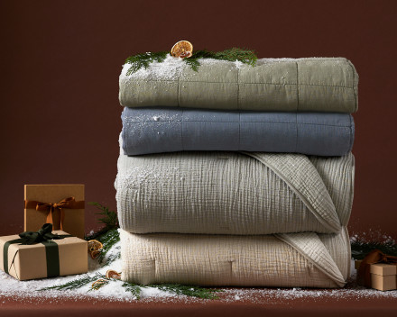 A festive stack of quilts with various colors and textures against a dark red background