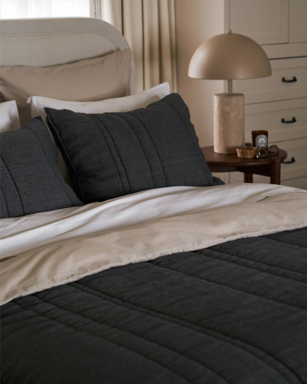 A bed made with charcoal grey shams and a quilt