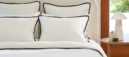 A neatly made bed with soft luxe white sheets with a soft black piping