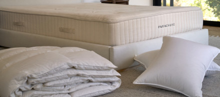 A down duvet insert and down pillow inserts on the floor next to a bed with a Parachute mattress