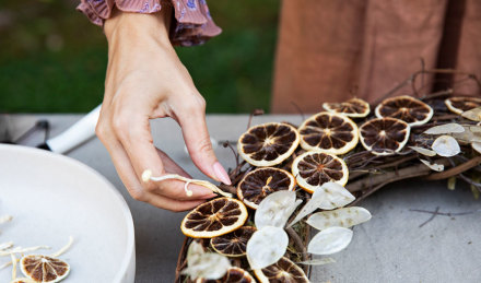 A woman laying out all of the citrus and leaves on the wreath. 