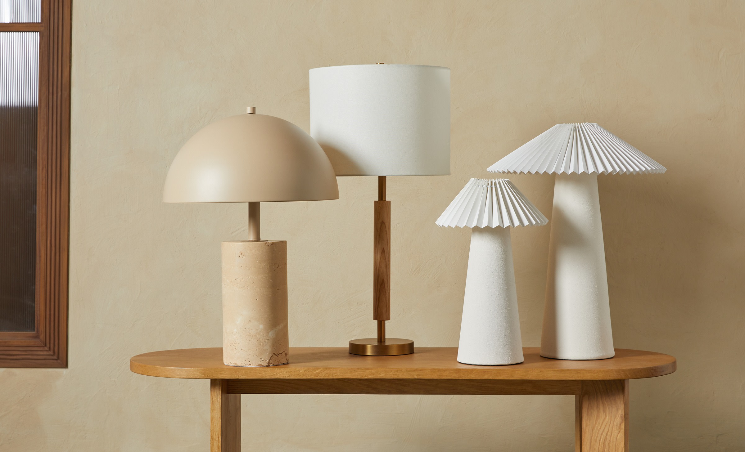 Four table lamps made of stone, porcelain, wood, and brass stacked on a white oak wood bench