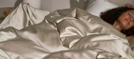 A person laying in a cozy bed with white and bone sateen sheets