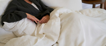 A person sitting in a cozy bed with cream linen sheets
