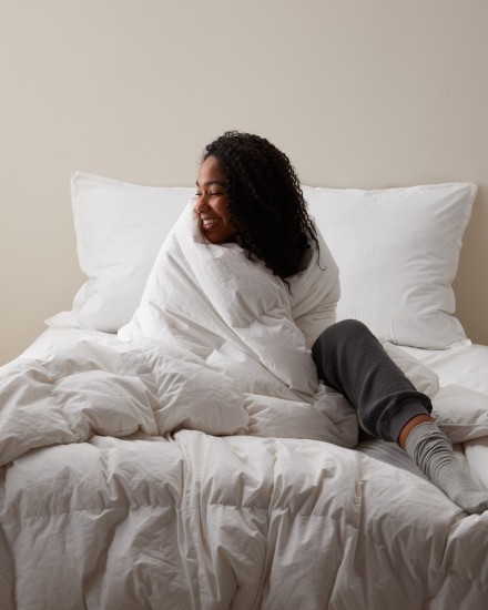 A person sitting on a bed with a duvet insert wrapped around their shoulders