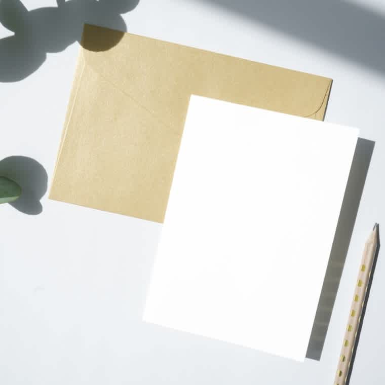 A pencil, letter envelope, and card are placed next to each other on a blank table.