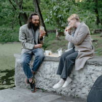 Two people are seen enjoying a meal together in a public park.
