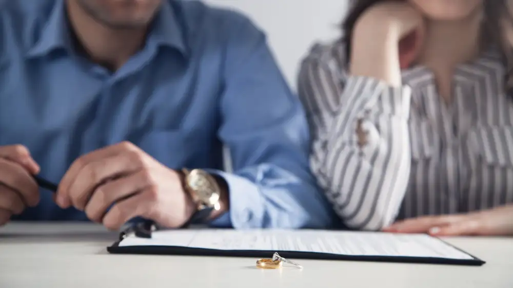 Relengage Marriage Ministry article photograph of a married couple looking at the wedding rings sitting in the center of the table in front of them, placed on top of divorce papers.