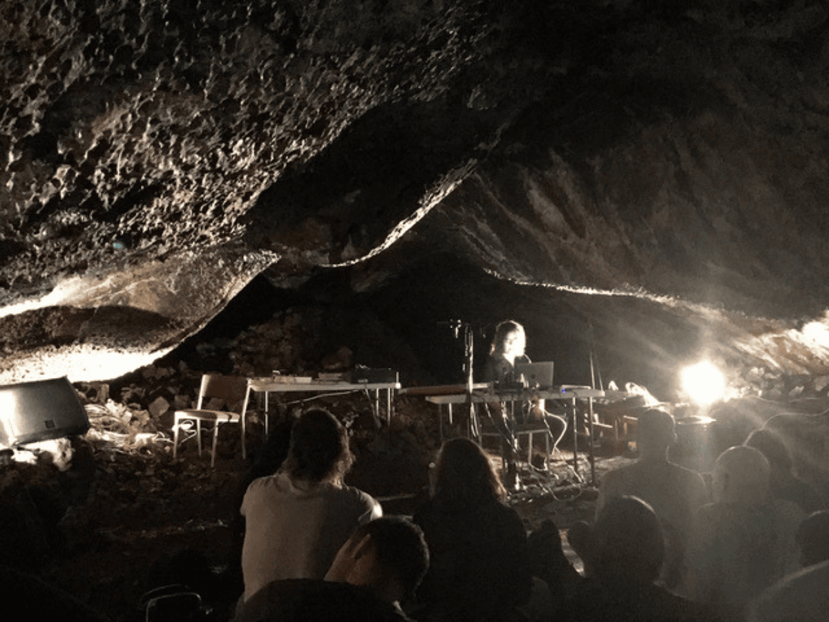 a photo of a person sitting at a table with a computer in a cave with some people watching.