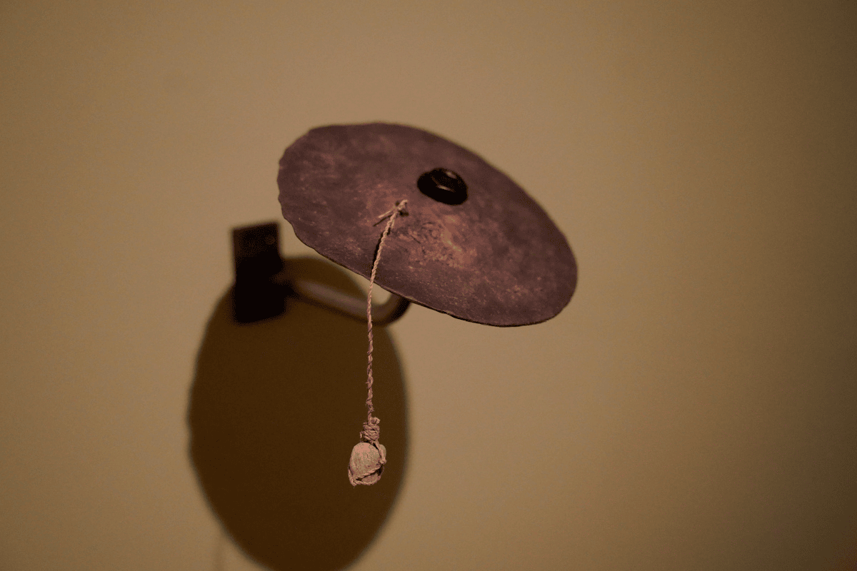 A close up photo of a cymbal-like object made out of bronze, tī kōuka and stone.