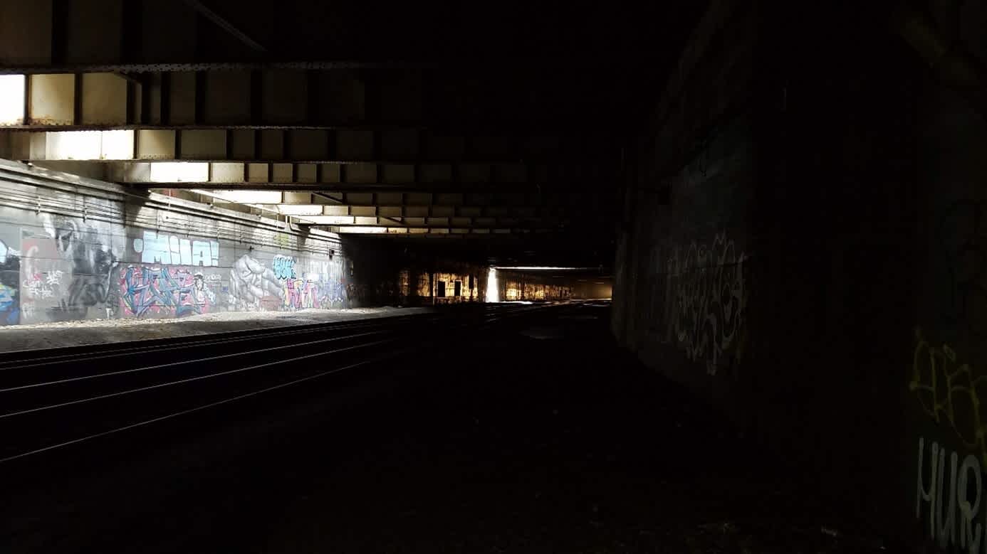 Dimly lit train tunnel with tracks stretching into the distance. Colourful graffiti on the left, distant light illuminating the tracks.