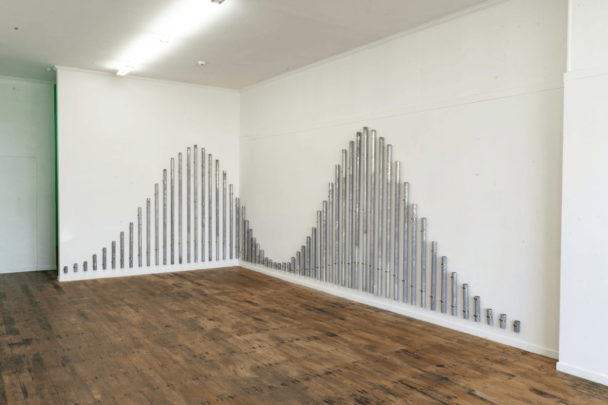 A photo of a gallery space with an installation made of aluminium pipes that mimic a tidal chart.