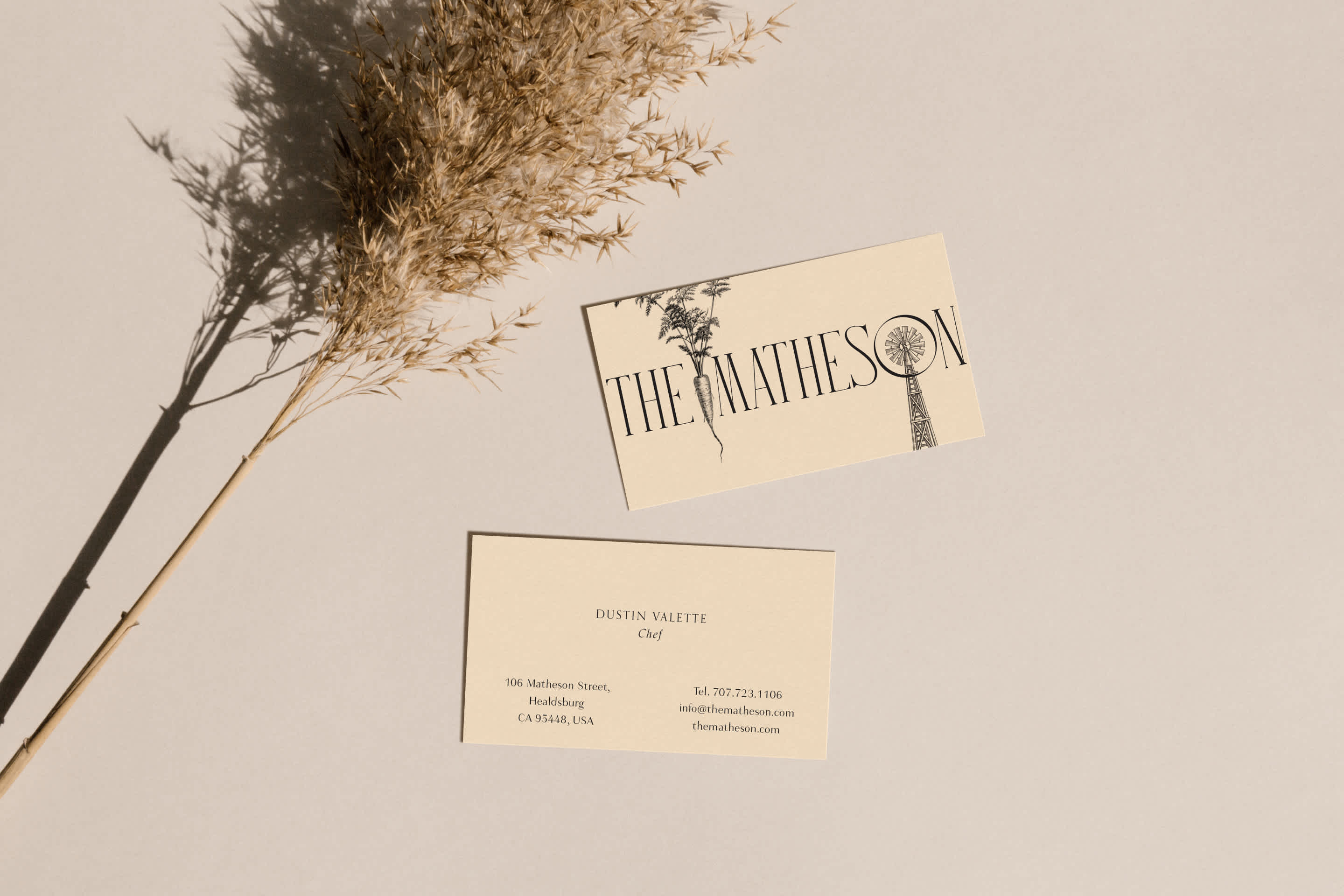 A couple business cards placed on the a table with some wheat on a stalk