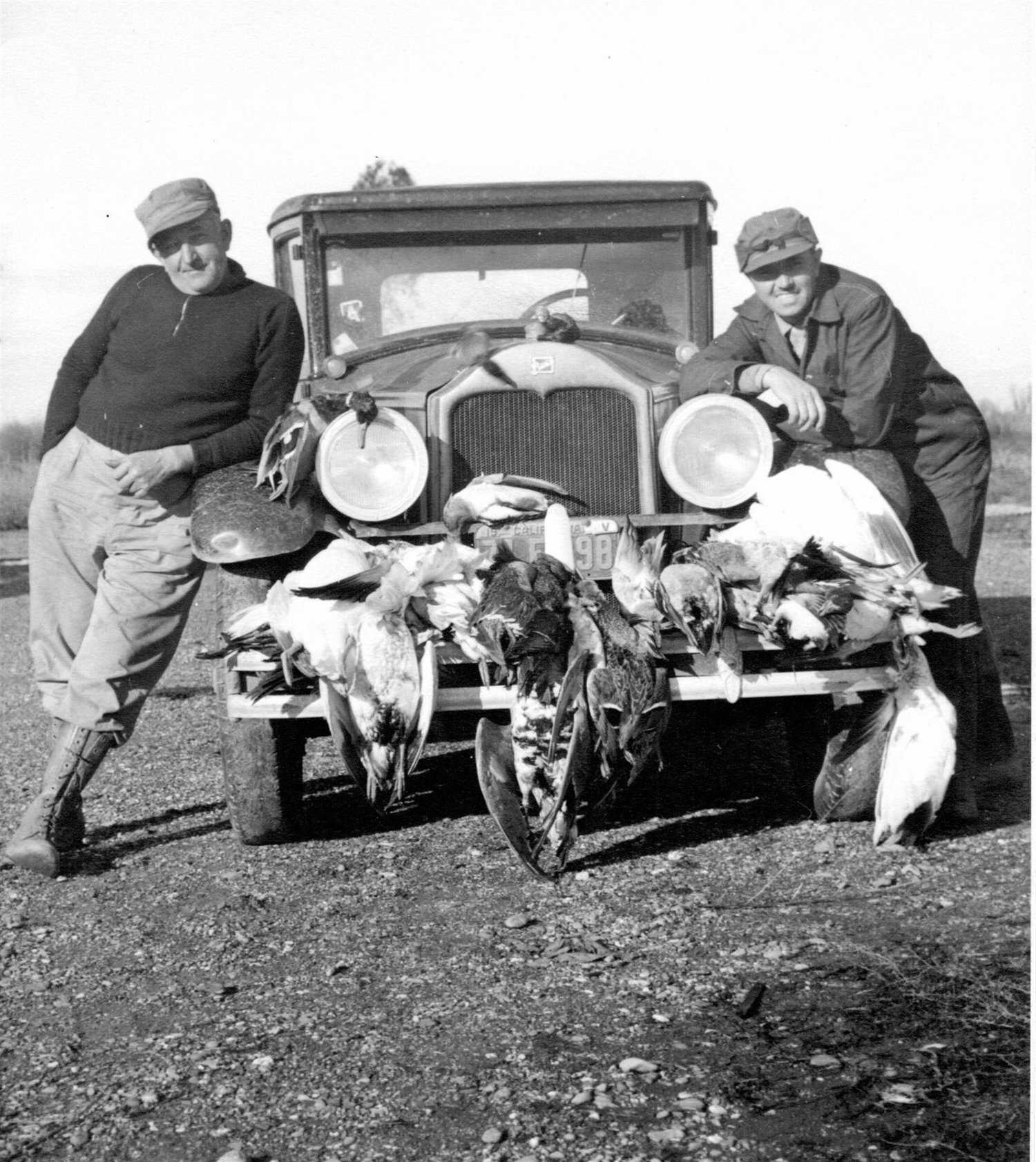 A historical photograph of marksmen returning with their haul of birds on the front of their primitive car.