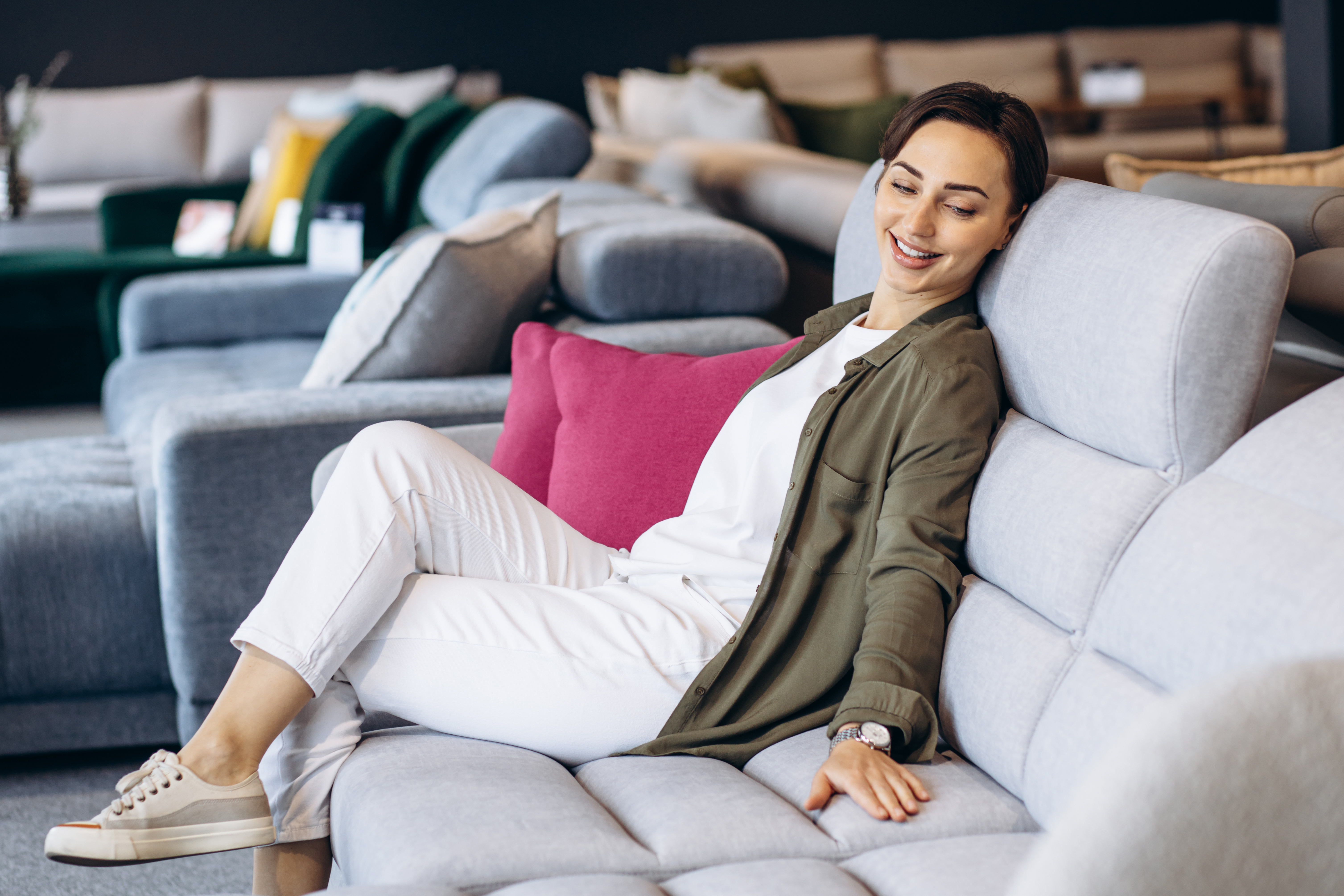 A customer happily testing out the feeling a piece of furniture in a store as she is shopping.