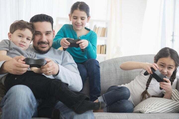 A father is sitting on a couch with his three children playing a video game.