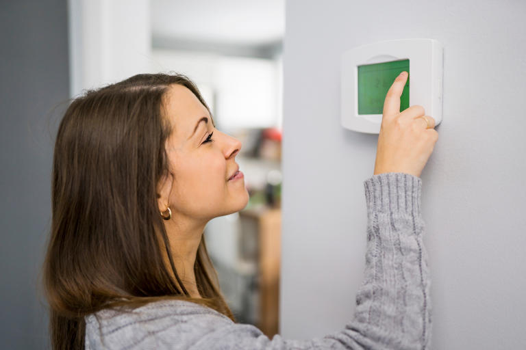 A young woman looking at her air conditioning unit in her home.