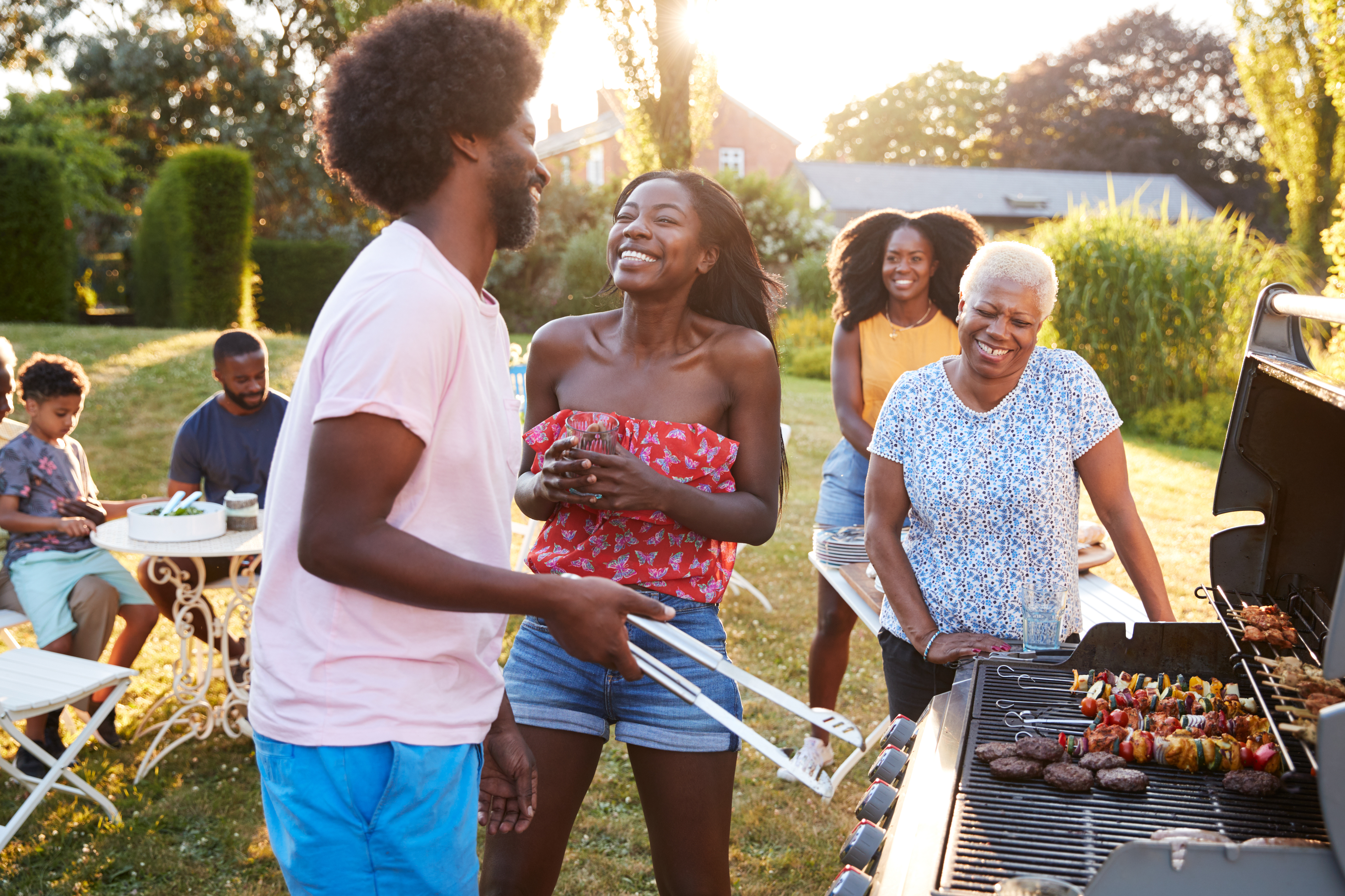 A family joyously spending time together outside for Memorial day while using a grill.