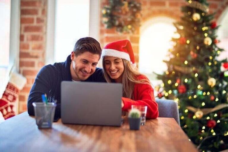 A couple is watching a laptop while sitting in a holiday festive room.