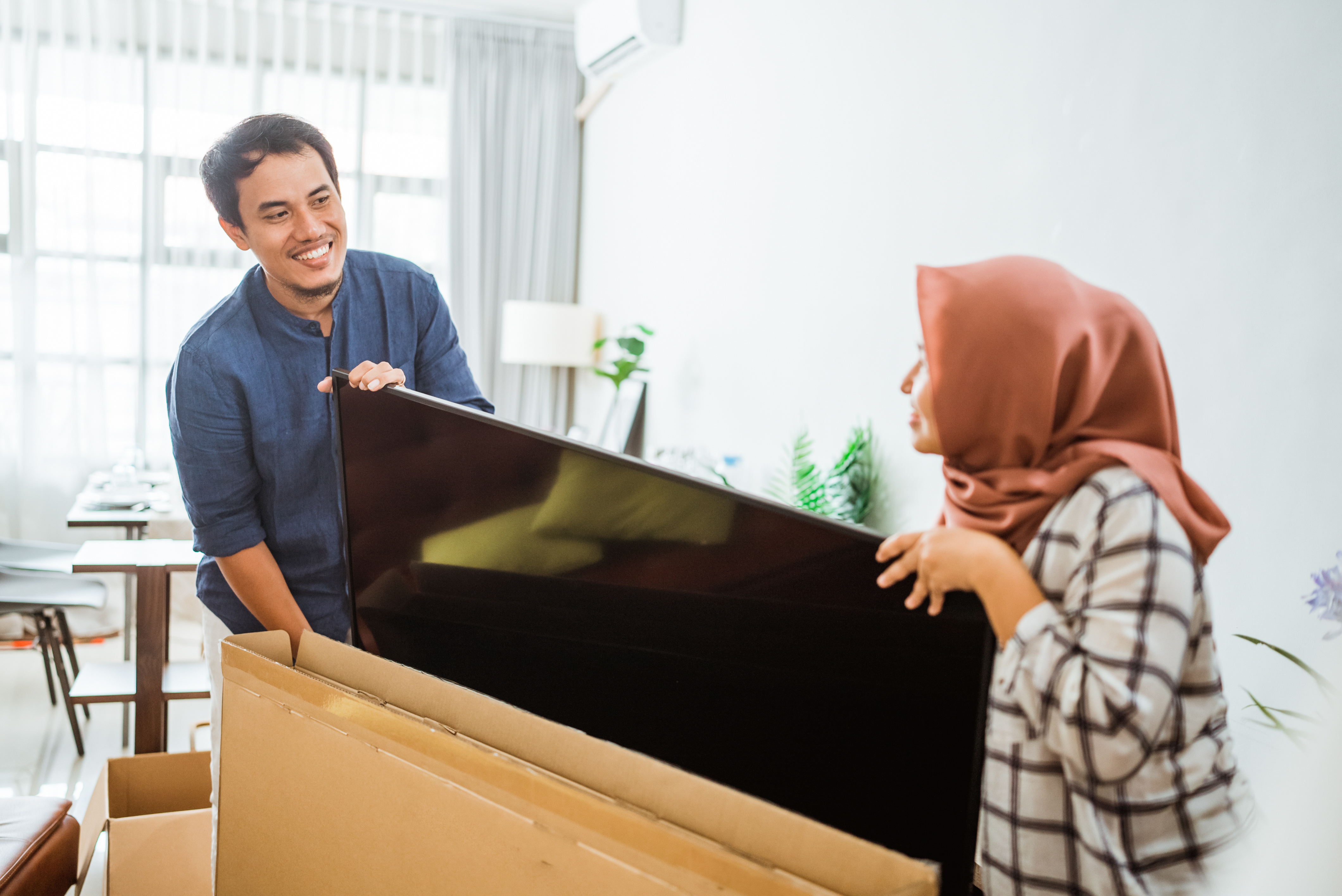 A pair of graduates setting up a Tv for their new home. 