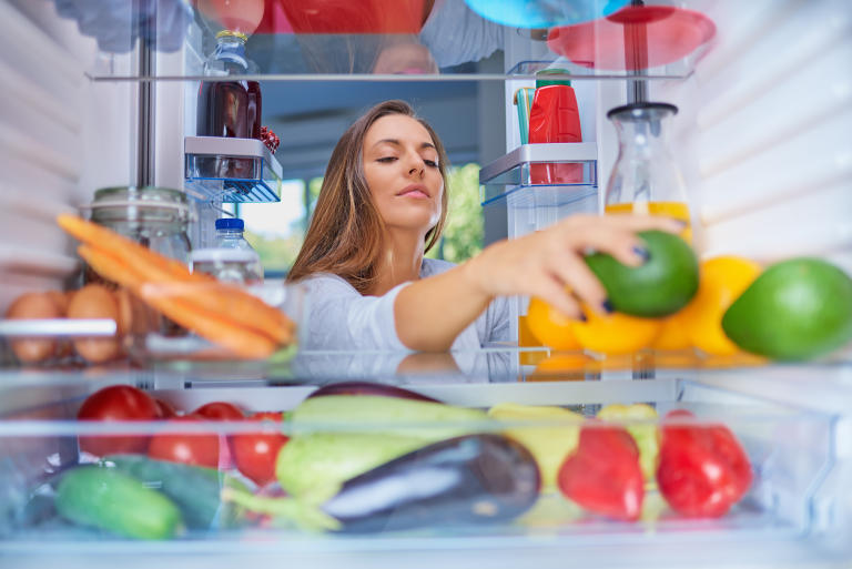 A woman reaches into a refrigerator to check and see what the temperature should be to store her food.