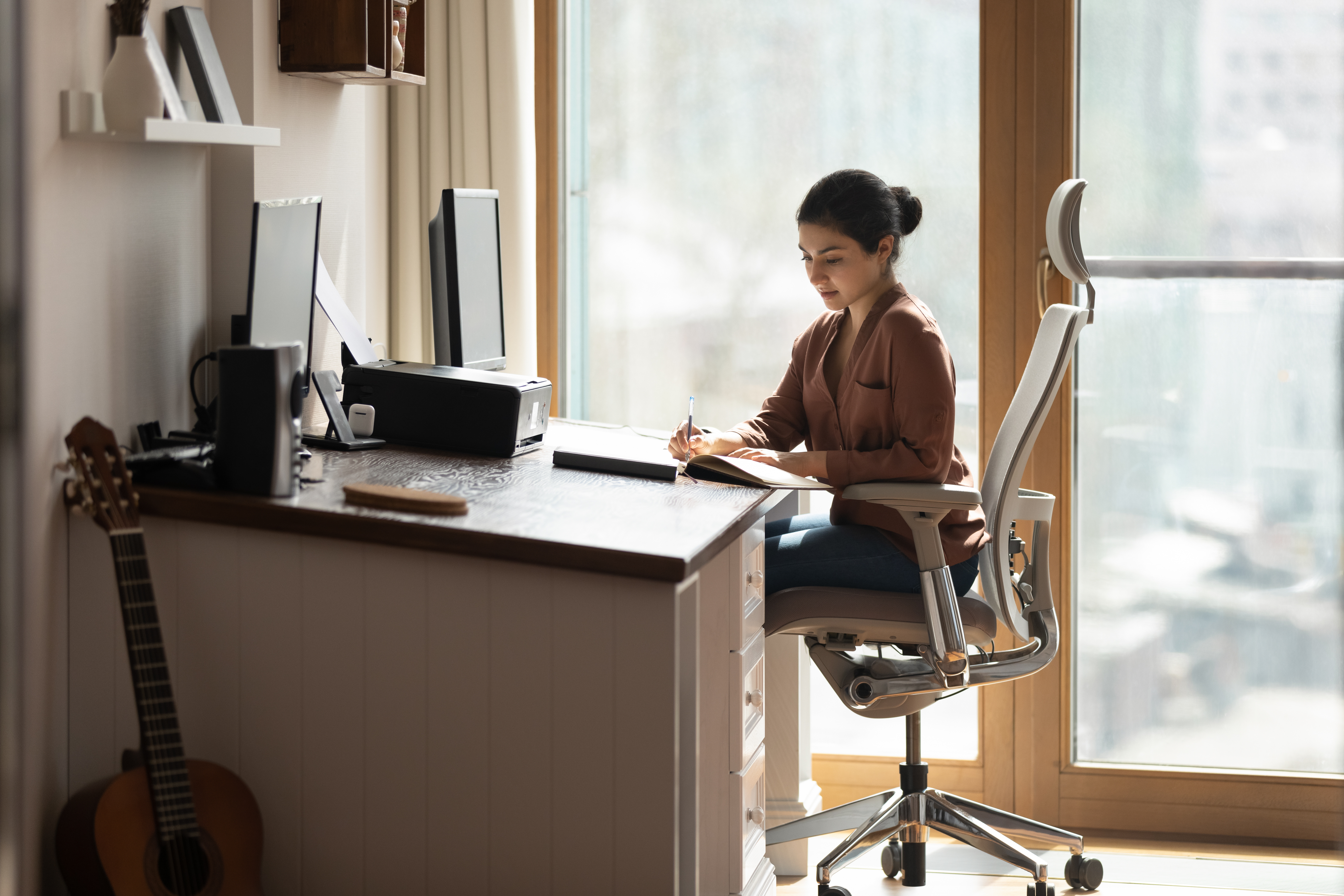 A young adult sitting at a desk in their home office in an office chair that supports their work needs.