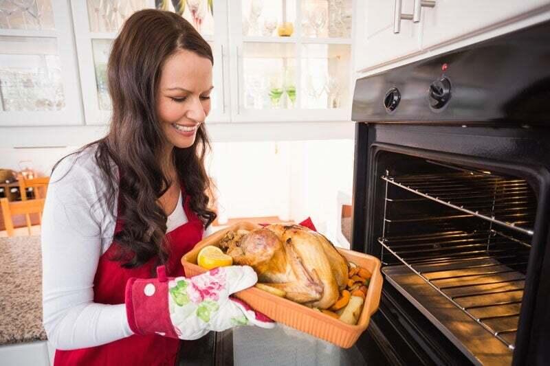 A woman is placing a turkey into the range in her kitchen.