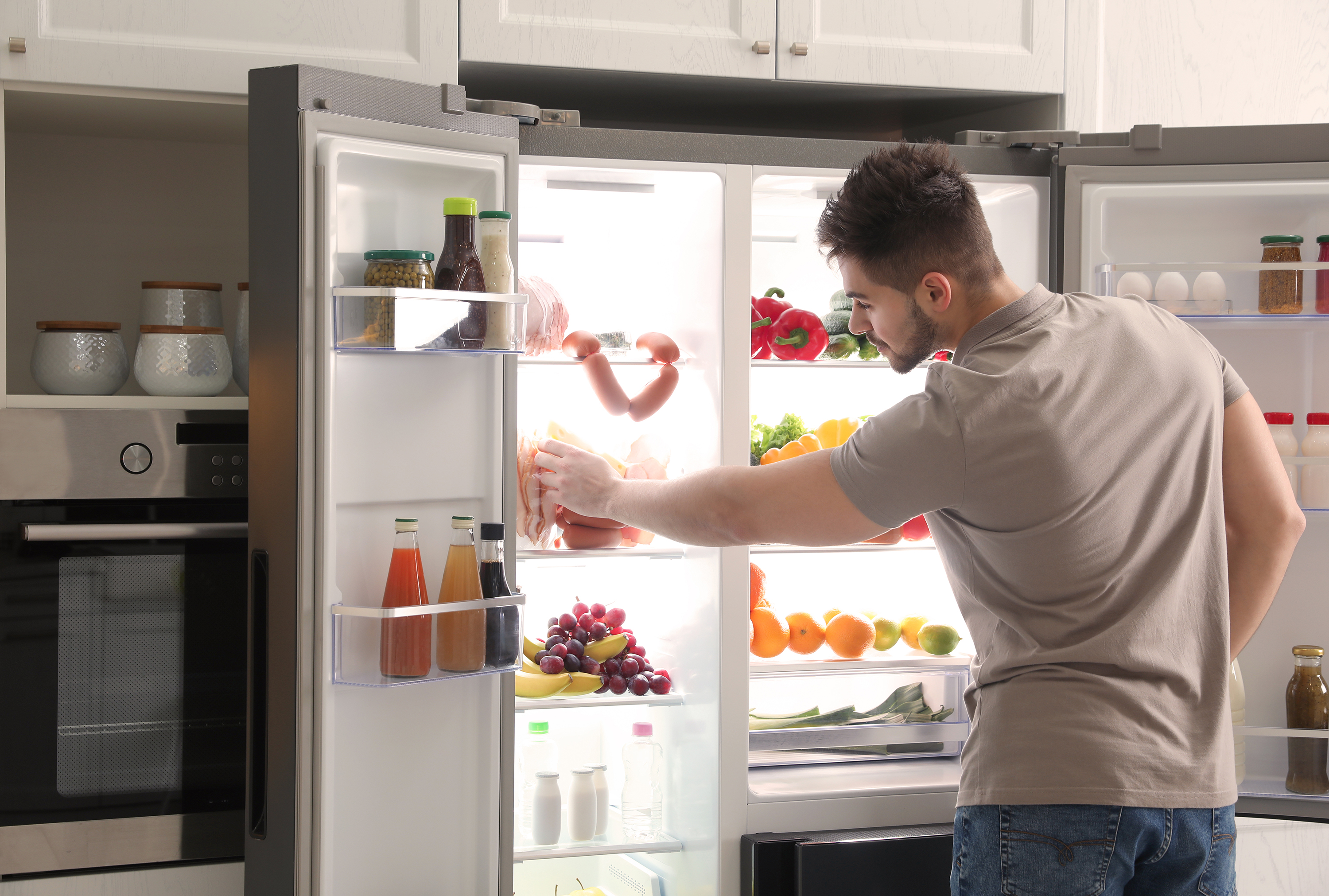 A young man pulling food from his stainless steel refrigerator showing the ease of filling your kitchen with the right appliances using Acima Leasing.