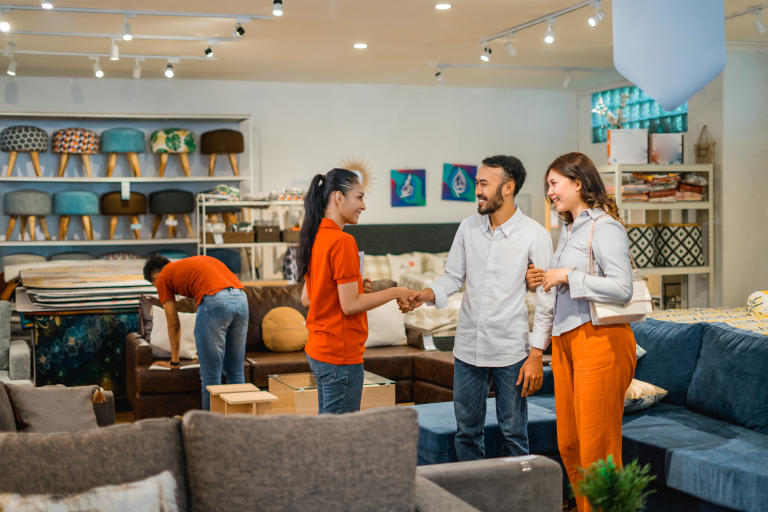 A smiling employee warmly engages with a happy couple, discussing furniture options for their home in the inviting atmosphere of the store.