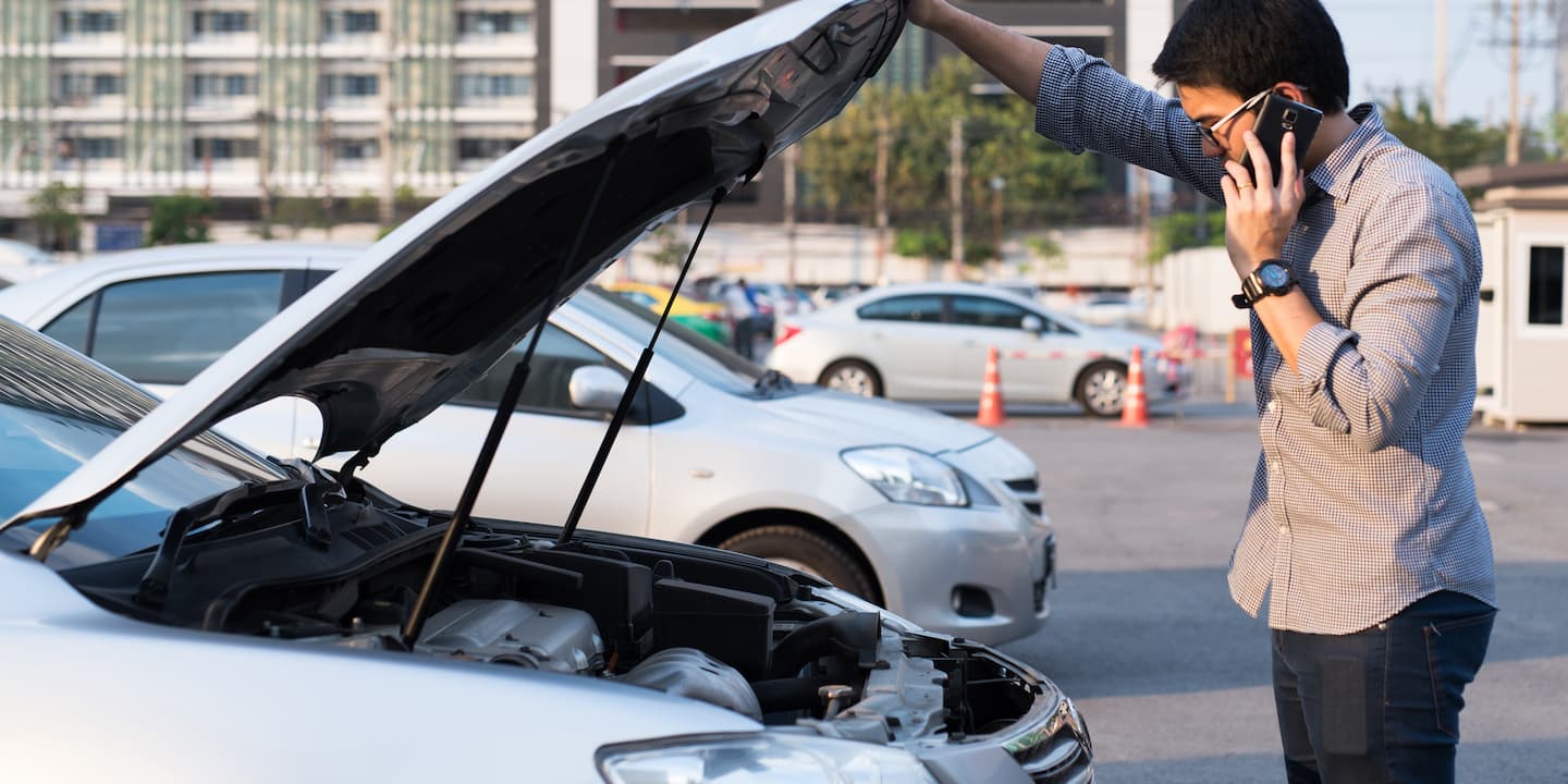 Man on the phone looking under the bonnet of his car. 