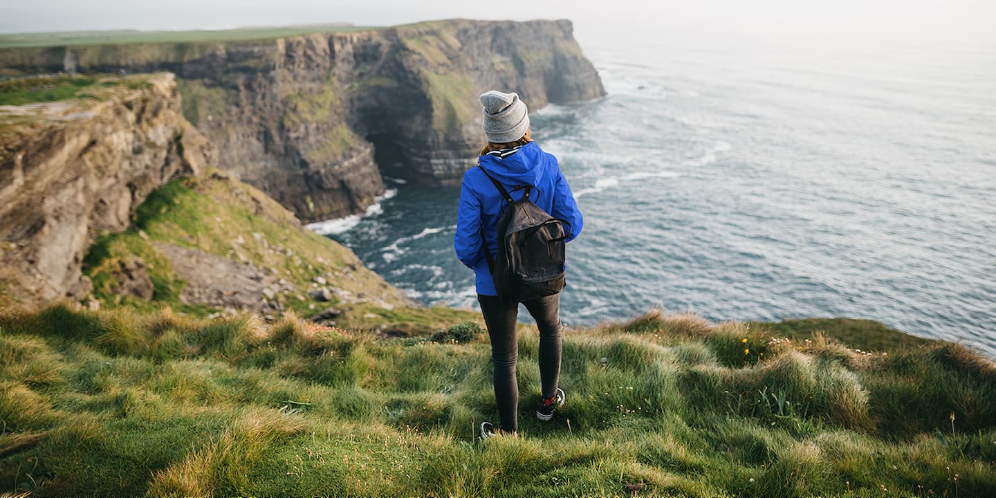 Women looking at sea from cliff edge in hiking clothes. 