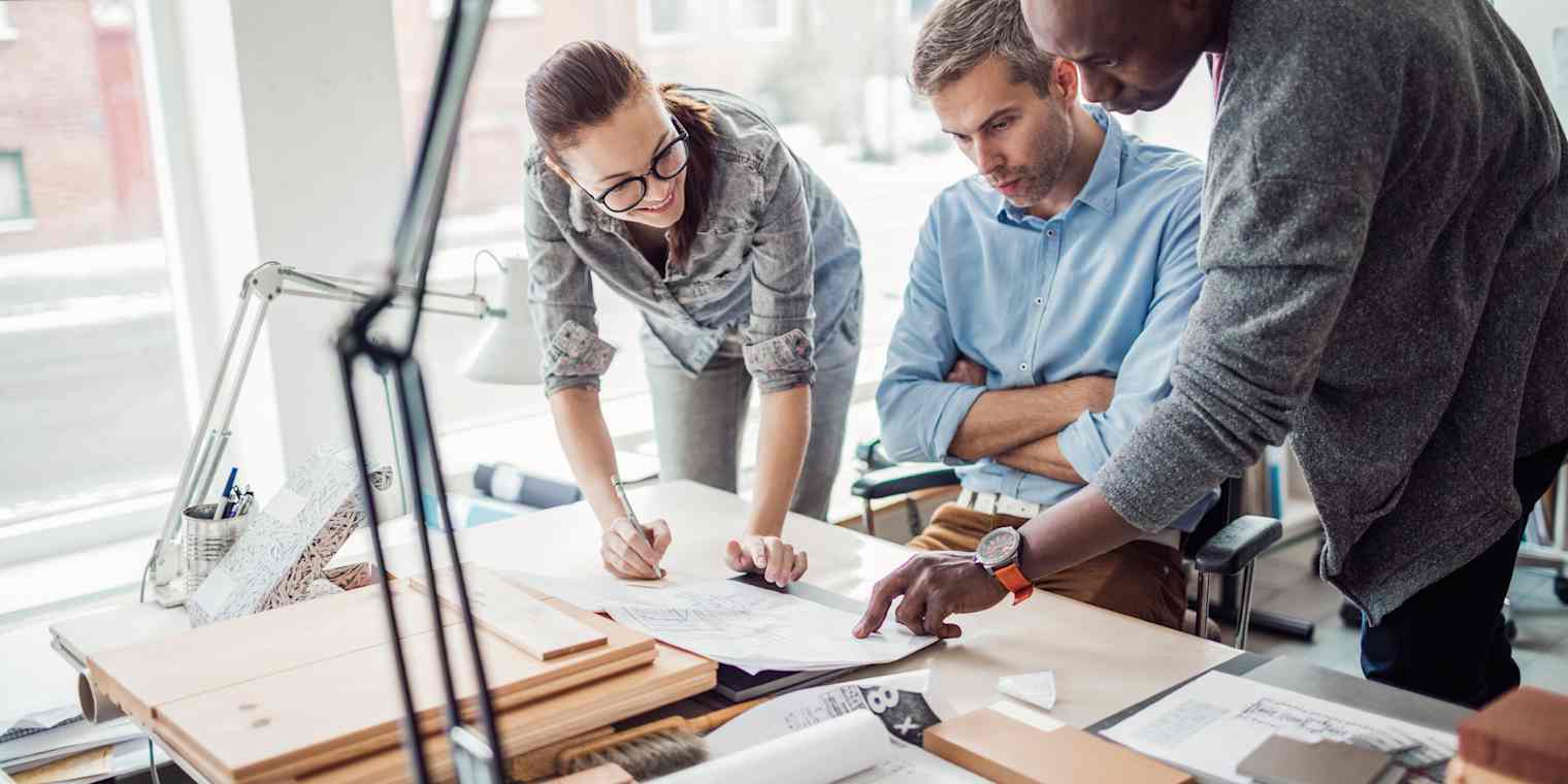 Two men and a woman review plans laid out on a desk.