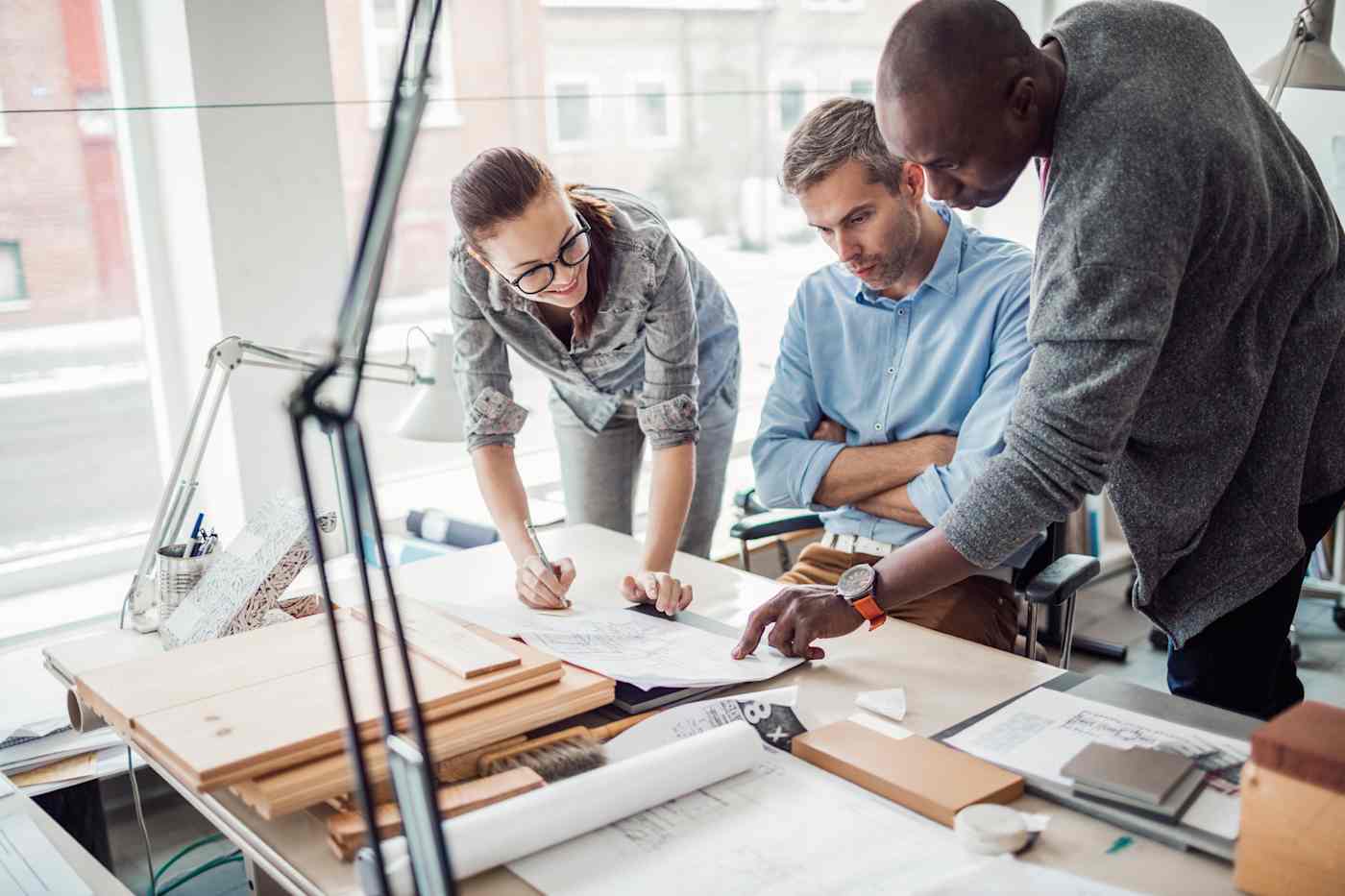 Two men and a woman review plans laid out on a desk.