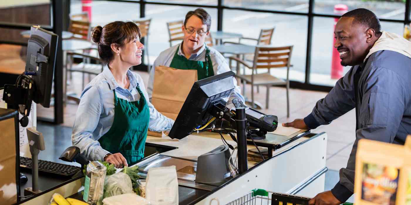 Hero image of three people at a grocery store checkout, laughing and talking to each other