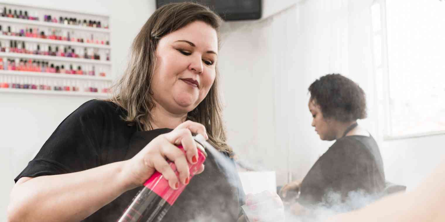 Hero image of a woman at a salon spraying hairspray