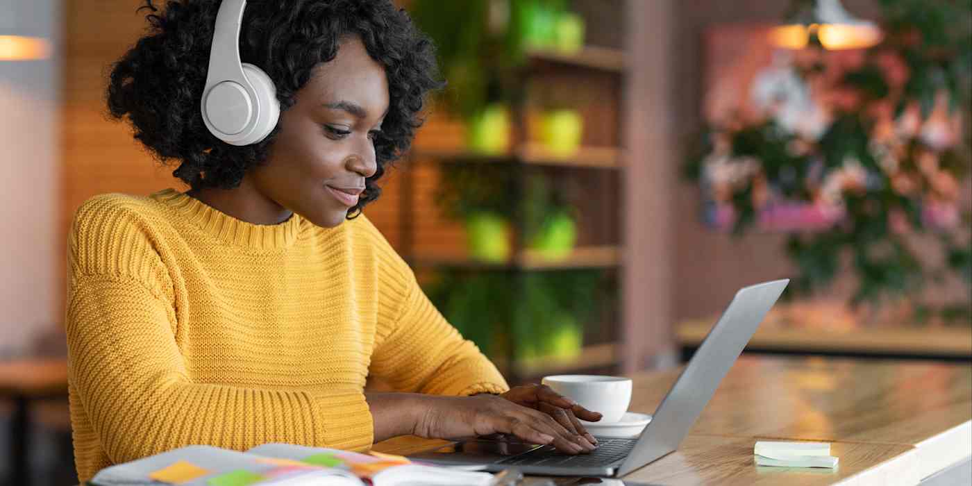 A woman works on a laptop while wearing headphones.