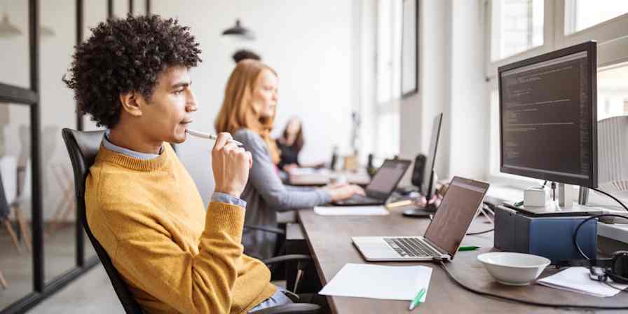 Hero image of a man sitting in front of a computer with code on the screen