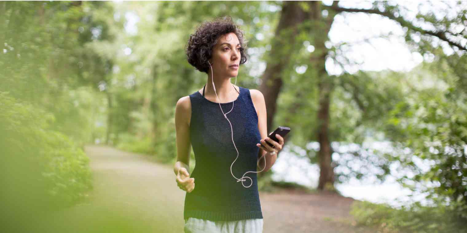 Hero image of a woman talking on the phone while walking with headphones in