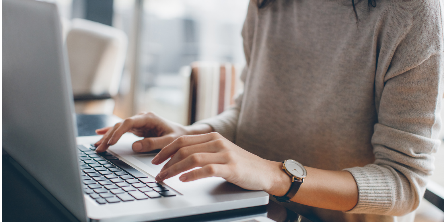 Hero image of a person's hands at a computer, wearing a sweater and a watch