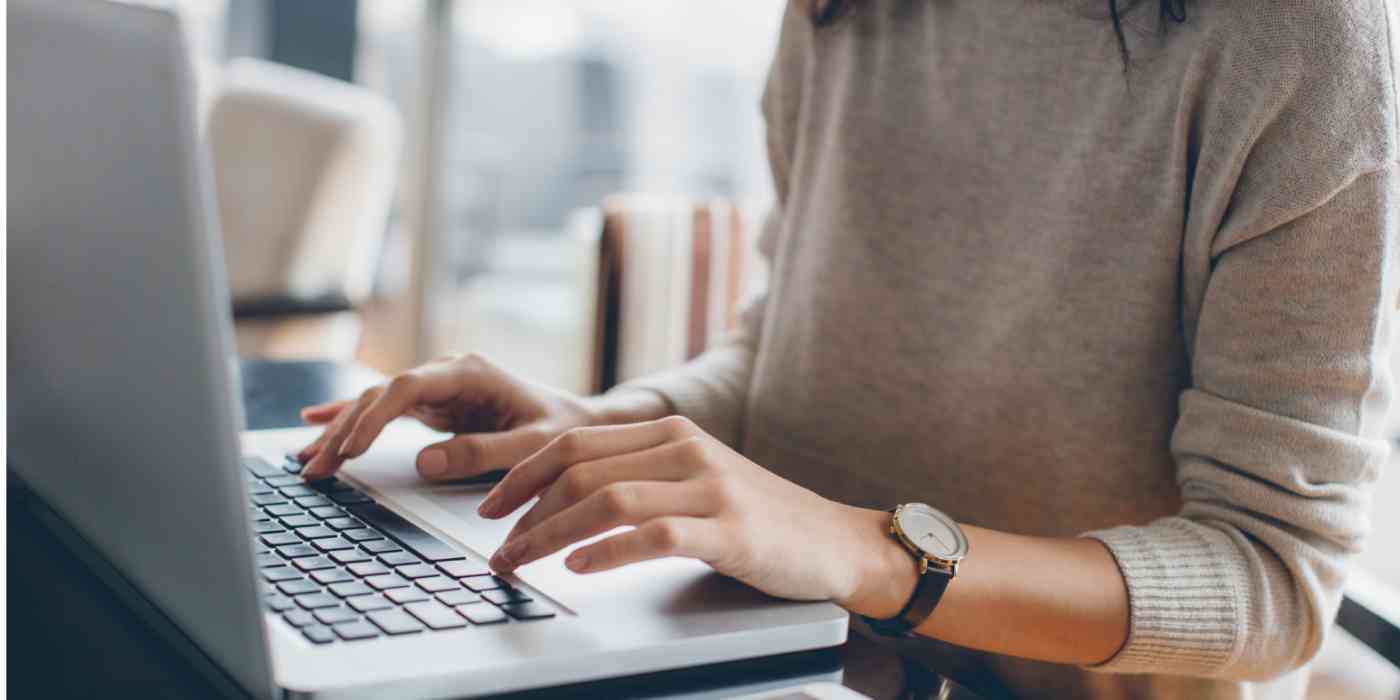 Hero image of a person's hands at a computer, wearing a sweater and a watch