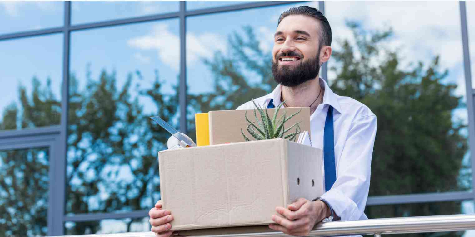 Hero image of a man smiling while holding a box of office supplies, with his tie undone (it looks like he just quit his job)