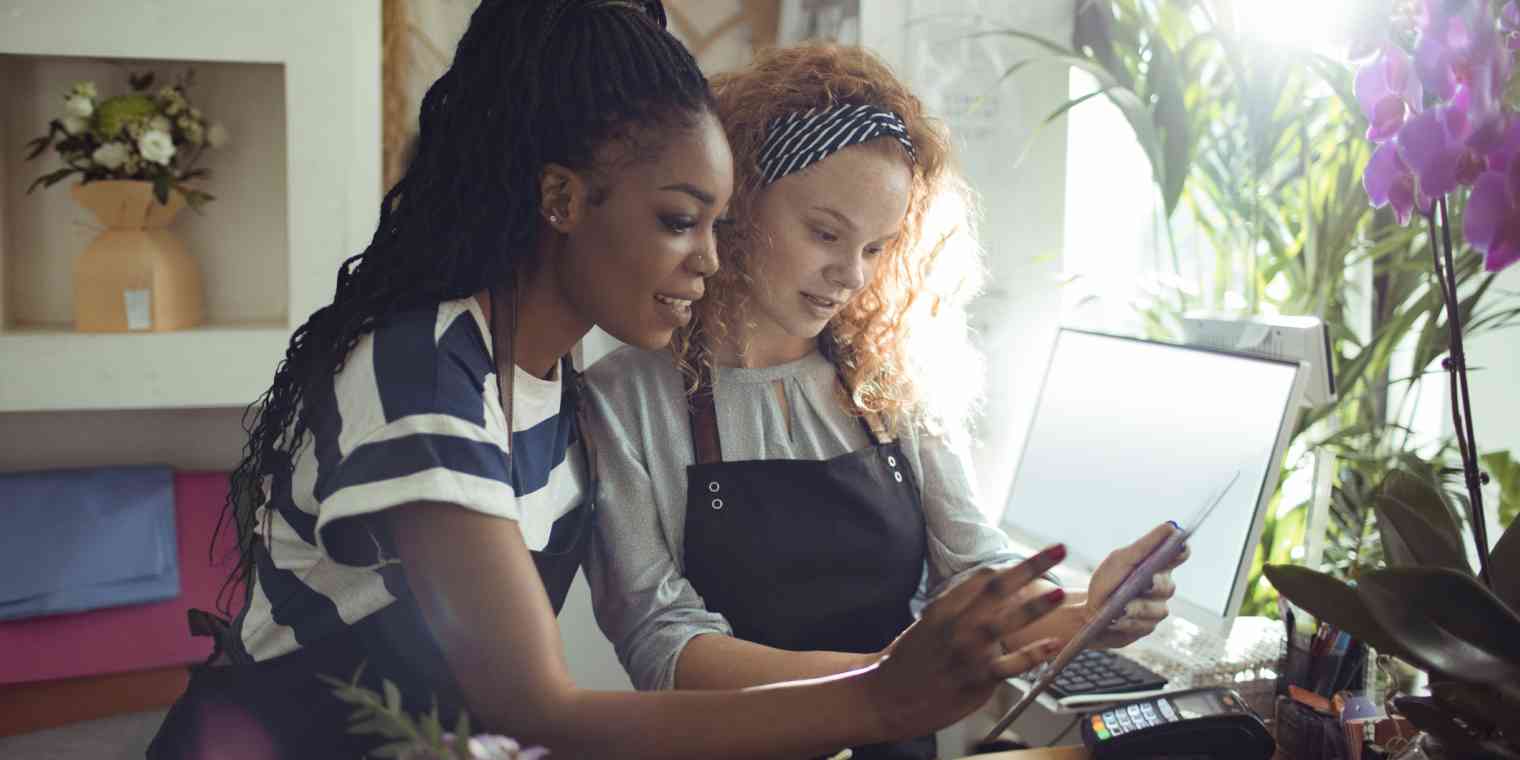 Two women in a flower shop looking at a tablet and computer.