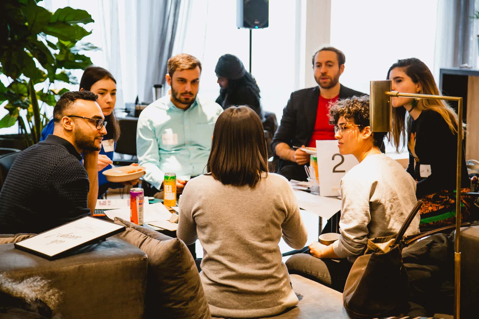 A group of people sit around a table talking at a business training event.