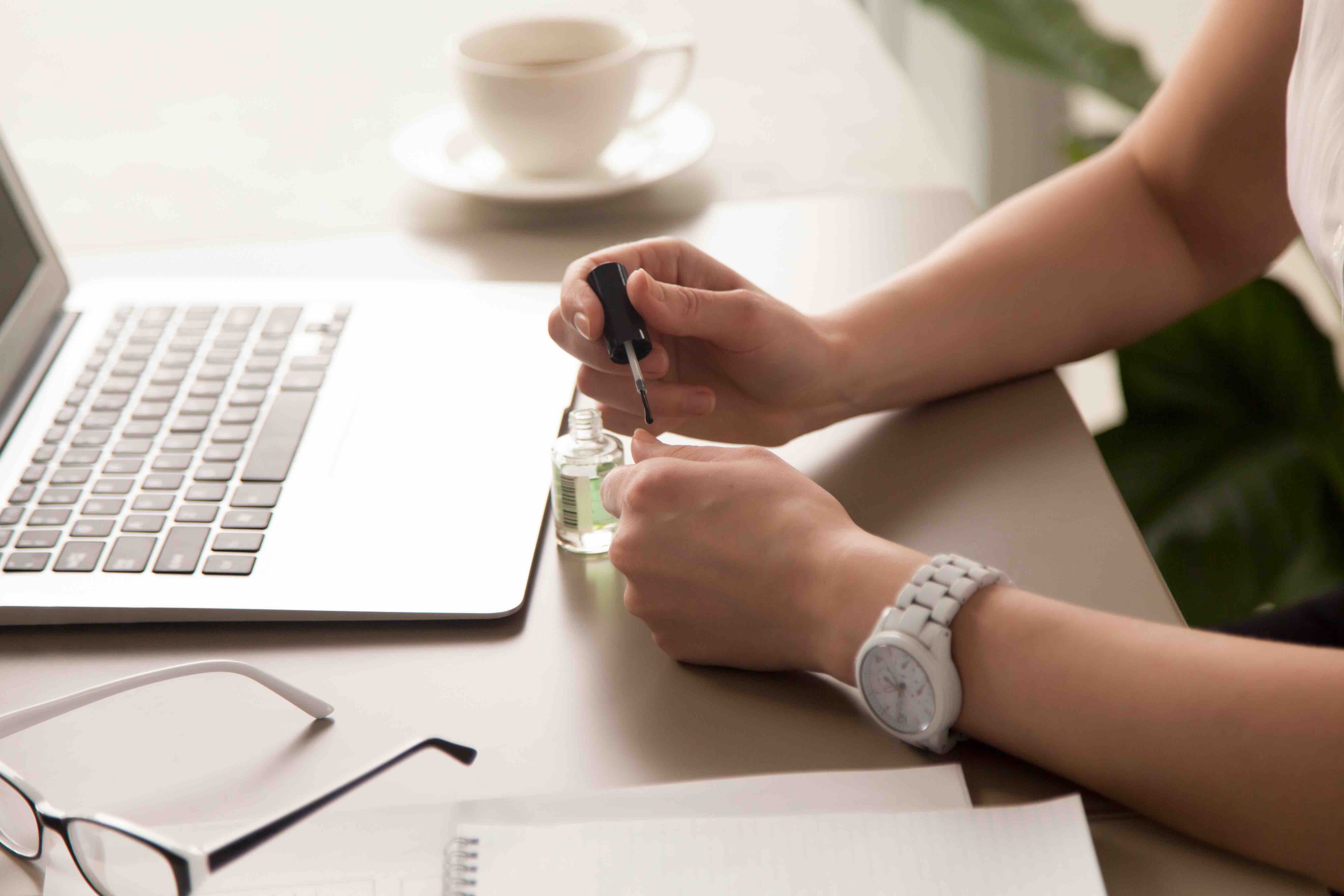 Person painting their fingernails instead of working at their computer
