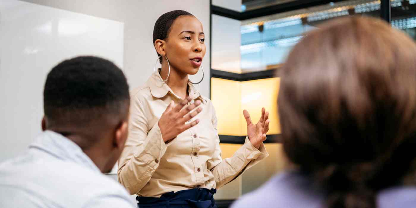 Hero image of a person speaking in front a group of other people in a small conference room