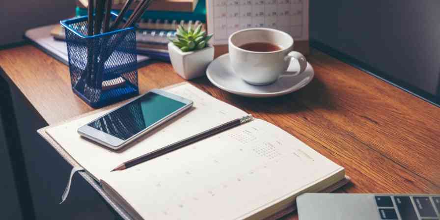 Hero image of a desk with a notebook, phone, tea, and pens